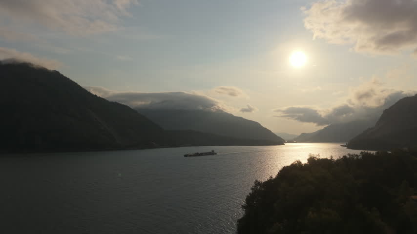 Silhouetted cargo barge traveling along the Columbia River after sunrise, framed by steep gorge cliffs, calm water, and warm morning light in the Pacific Northwest.