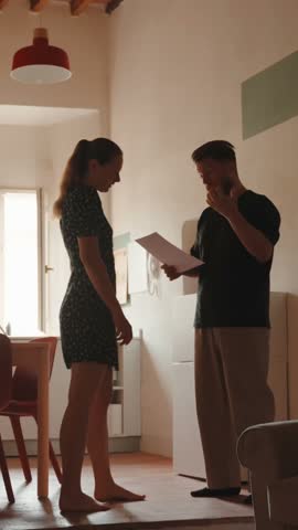 Frustrated man reading a document and arguing with his upset wife about financial problems, the woman getting distressed and leaving the room after their intense discussion. Vertical video