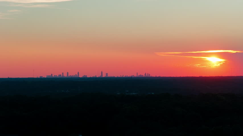 Atlanta skyline sunset aerial, downtown and midtown towers silhouetted against an orange sky above dark forest canopy, Georgia, Southeast USA