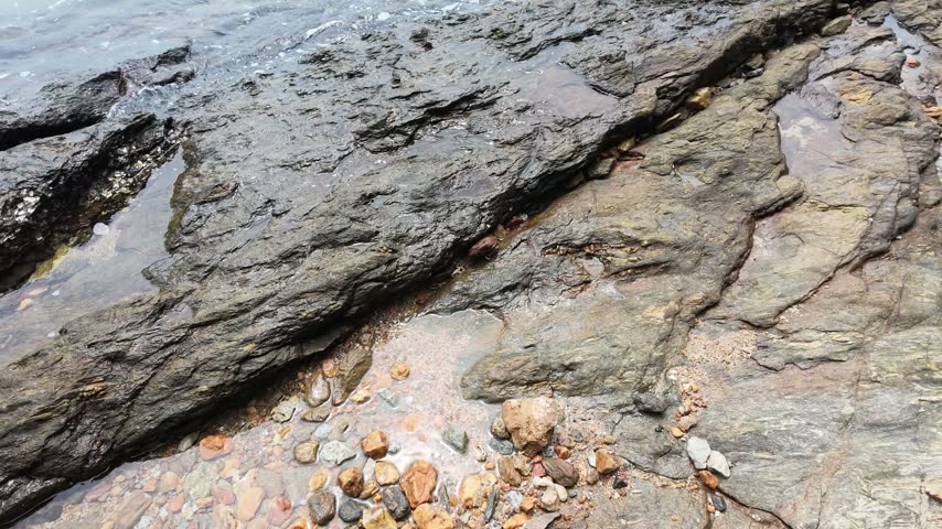 High-angle view of textured coastal rock formations and pebbles along the shore in Rayong, Thailand.