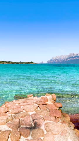 Vertical POV walk along a stone pier at Porto Istana, Sardinia, with the Mediterranean Sea surrounding the rocky coastal structure in a scenic travel setting.