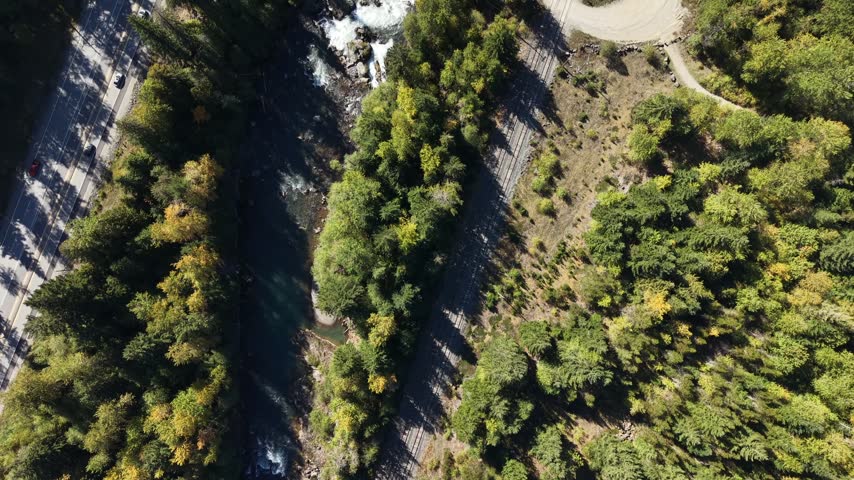 Forward tracking top down shot over dense forest revealing a turquoise river with white water rapids and roads on both sides, Squamish, British Columbia, Canada.