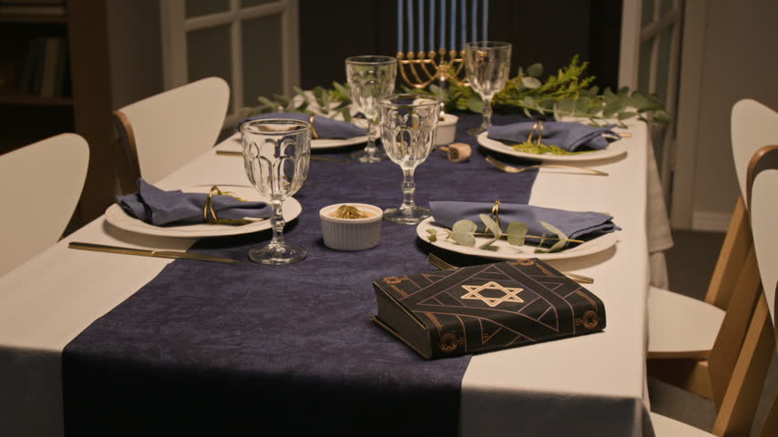 Hanukkah holiday dining table decorated with festive tableware, prayer book and Menorah. Footage suitable for Jewish cultural holiday advertising and promotional campaigns
