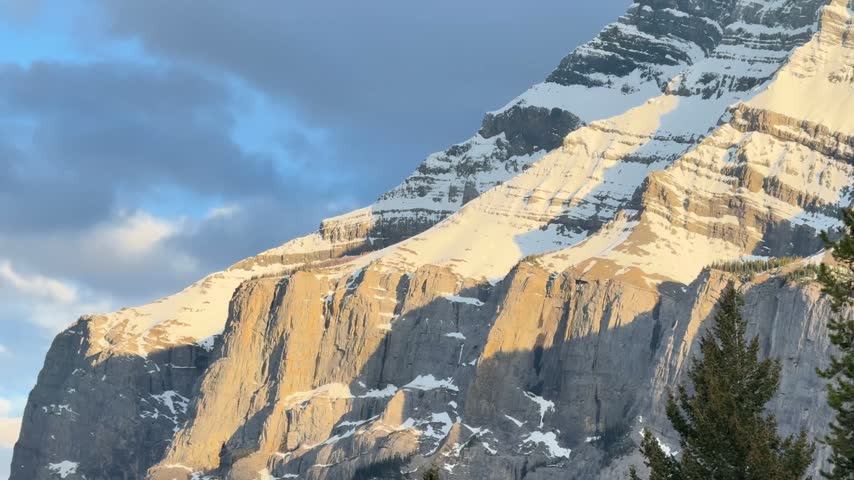 Handheld shot of snow-capped mountain peaks at Tunnel Mountain, Banff National Park, under partly cloudy sky with natural lighting.