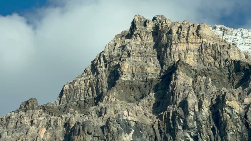 A slow handheld push in and tilt down across a rugged mountain peak under a partly cloudy sky near Field.