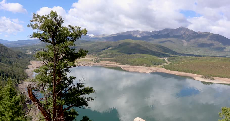 Static video of Dillon Reservoir from Sapphire Point Overlook. There is a tree in the foreground and mountains in the background.