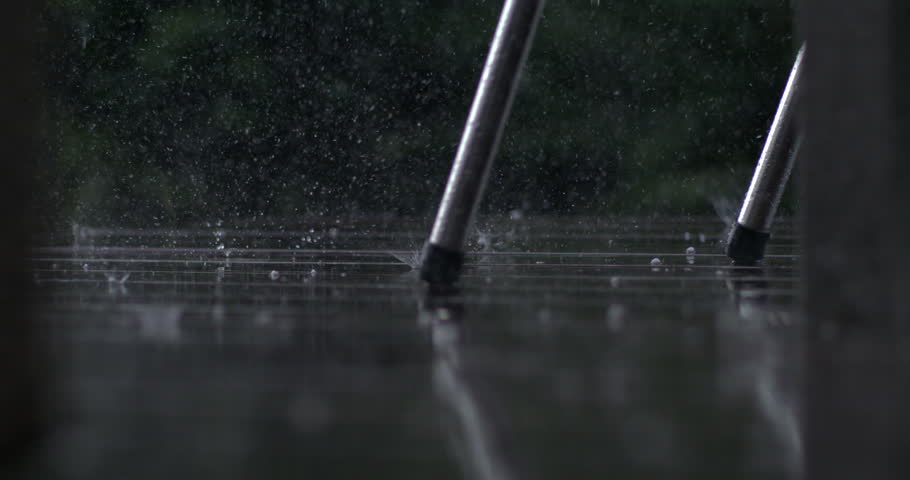 Low angle view of rain splashing around chair legs on wet wooden deck, captured in super slow motion with high speed camera, moody and reflective scene