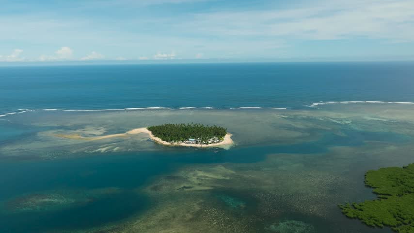 Tropical island with white sand in coastline. Coral reefs in turquoise water with waves. Mindanao, Philippines.