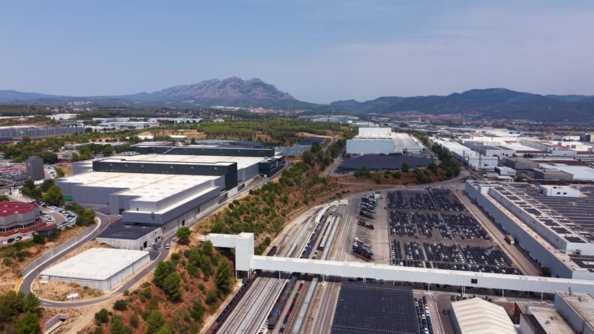 Overhead view of a large automotive manufacturing complex with railway tracks, car storage lots, warehouses and mountain backdrop in a Spanish industrial area