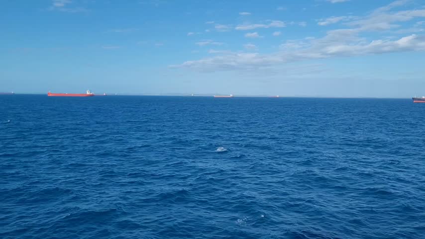 Multiple large cargo ships and bulk carriers anchoring offshore at Gladstone Port Australia waiting in queue to berth, busy anchorage area with vessels on horizon over blue ocean.