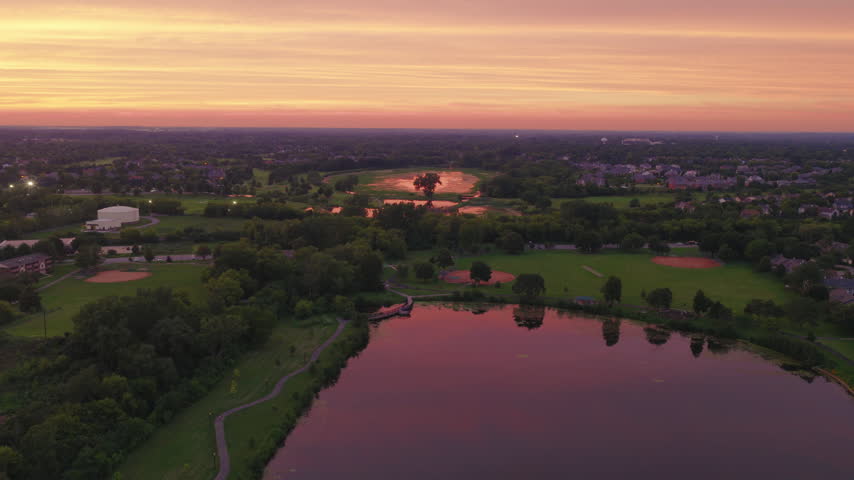 Suburban pond mirroring an orange sunset sky in Vernon Hills, Illinois, with parkland, homes and tree lined shoreline in the warm evening light.
