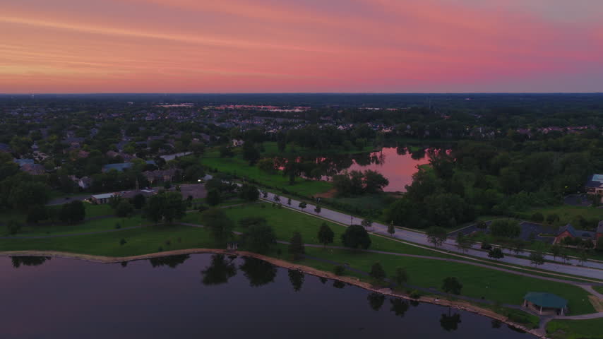 Suburban lake sunrise aerial in Vernon Hills, Illinois, calm water reflecting a pink and orange sky above a neighborhood park and homes, Chicago suburbs, Midwest USA