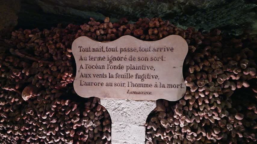 French poem inscription by Lamartine stands before tightly packed bones inside the dim Paris Catacombs corridor.
