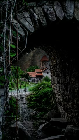 Milky Way Galaxy view through a rustic stone arch framing an ancient building and green landscape. Armenian apostolic church. Starry night sky. Monastery complex