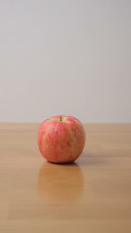 Person holding fresh ripe red apple on wooden table close up