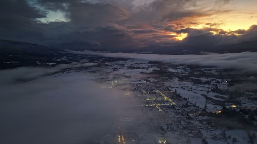 Aerial view establishing panoramic of the town of Melipeuco, Chile, completely covered in snow, with an epic sunset in the background among the clouds