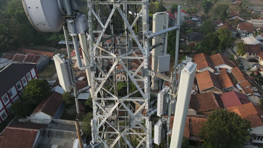 Aerial view of a telecommunications tower with various antennas rising above residential rooftops in Cilongok, Central Java, Indonesia.