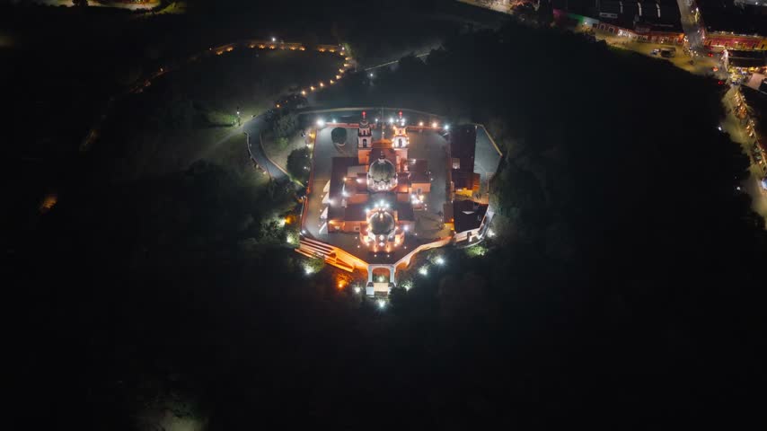 Aerial view of the illuminated Santuario de la Virgen de los Remedios at night, perched on a hill in Cholula, Puebla, Mexico.