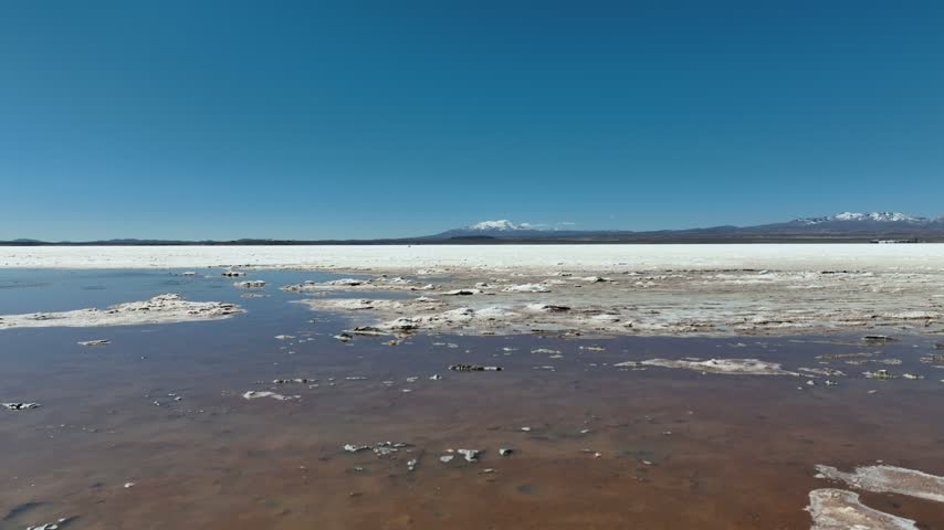 Aerial view of the vast white salt crust and shallow water of Uyuni Salt Flat under a clear blue sky in Potosi Department, Bolivia.