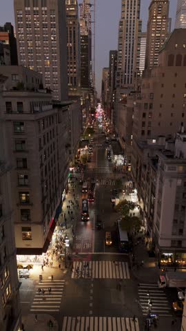 Vertical video of the Fifth Avenue in Manhattan bustling with yellow taxi cabs and pedestrians shopping. Rockefeller Center shines in the distance in this iconic NYC location