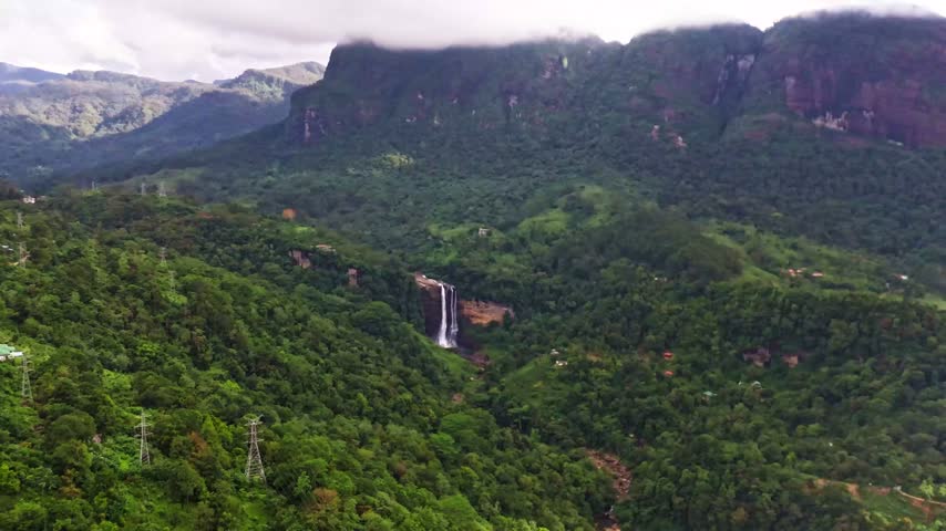 Cinematic drone hyperlapse of Lakshapana Falls in Sri Lanka, with water cascading down the mountain while clouds move rapidly across the sky, creating a dramatic natural scene.