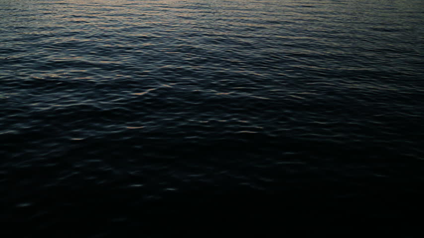 Tilt from the water to the Krk Bridge during dusk with a lake and small boats in the water.