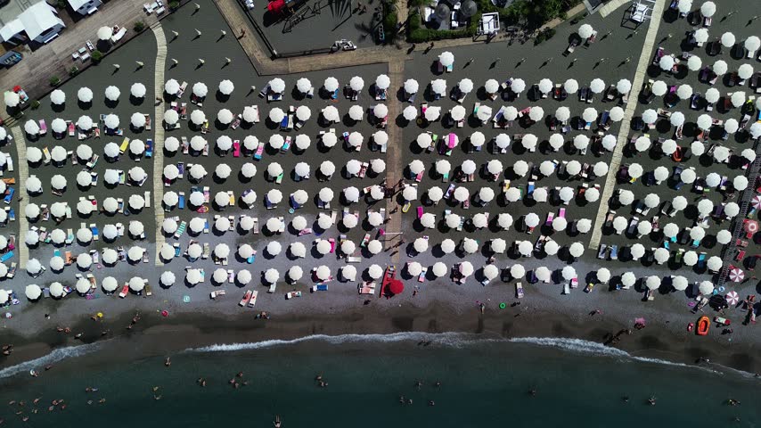 Aerial view of a crowded beach with rows of white umbrellas and people swimming in the sea in Sorrento, Campania, Italy.