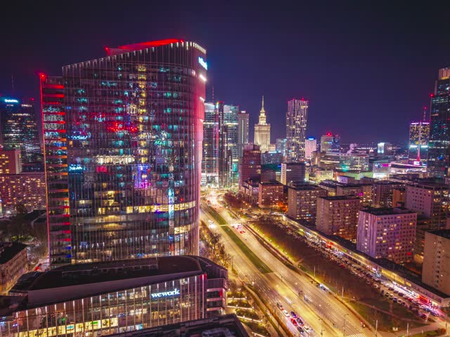 Aerial view of the illuminated Warsaw skyline at night featuring the Palace of Culture and Science and modern skyscrapers above the city streets in Warsaw, Poland.