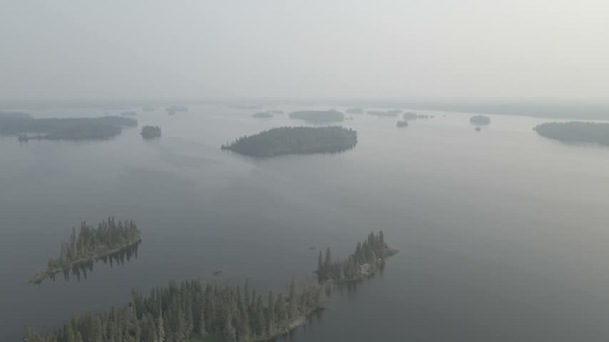 Drone flying over a large calm lake with many small islands all covered in fog or smoke
