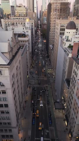 Vertical screen panning up reveals Fifth Avenue in Midtown Manhattan, New York City. Cars traverse street below and sun sets, casting a warm glow over the urban landscape