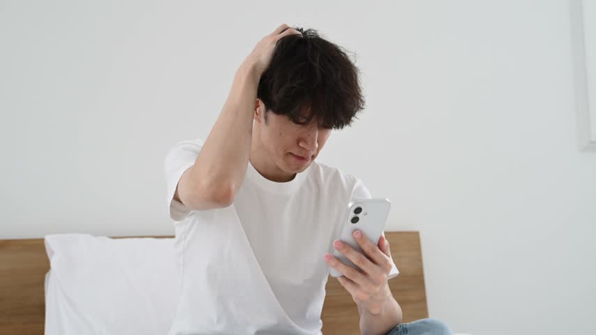 Japanese Man in His Thirties Looking Worried While Using a Smartphone
