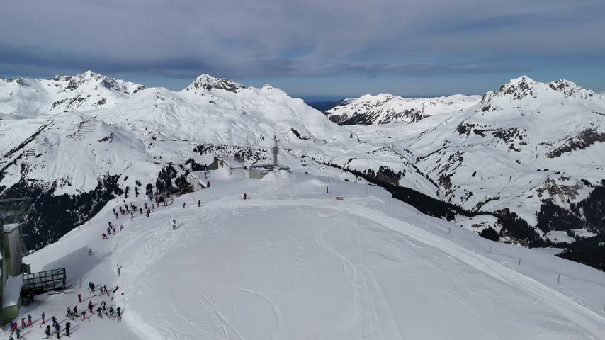 Aerial view along a snowy mountain ridge with avalanche barriers and a winding ski trail.