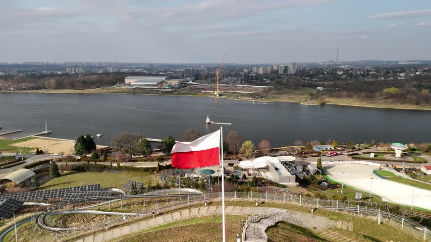 Aerial view of a Polish flag above park grounds and a lake on a clear day.
