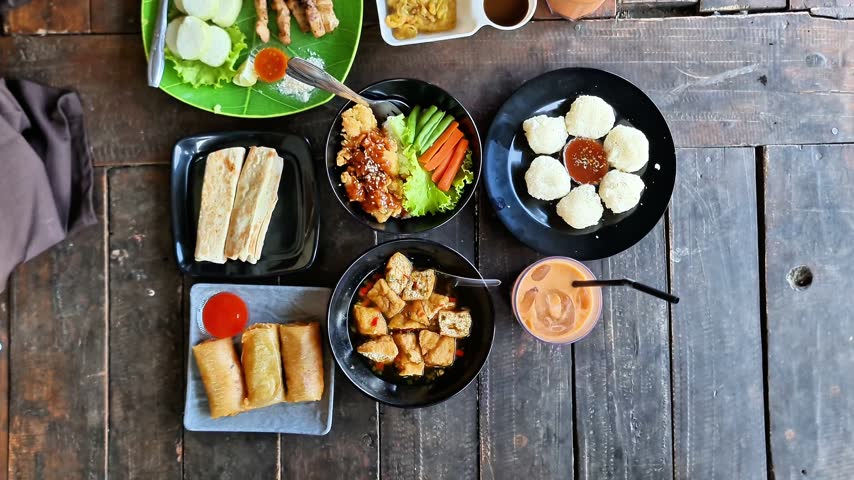 Close Up of Delicious Indonesian Street Food Feast with Chicken Satay, Peanut Sauce, Rice Cake, and Fried Snacks on a Wooden Table