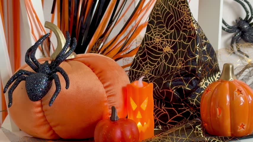 Halloween decor still life with pumpkins, glitter black spider, witch hat with golden web and LED jack‑o’-lantern candle