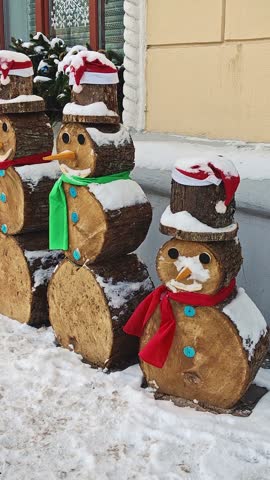 Decorative wooden log snowmen with hats and scarves on snowy street. Concept of eco-friendly Christmas outdoor decoration