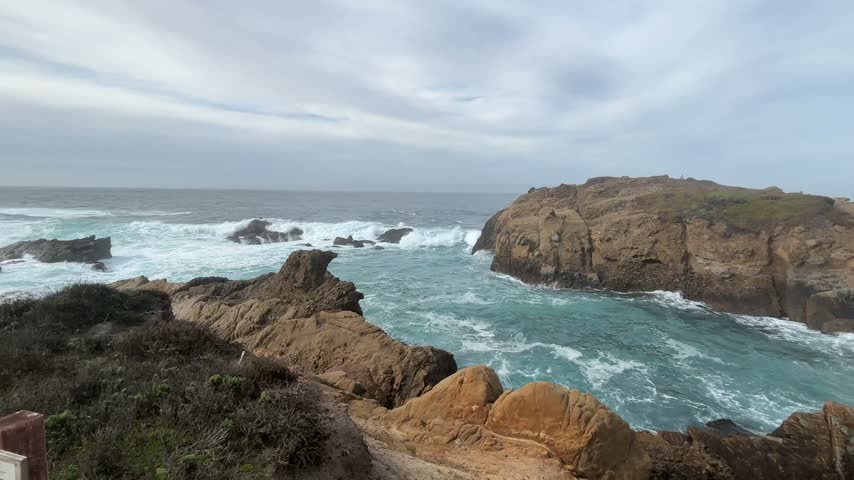 Ocean waves swirling around rugged rock formations along the California coast on an overcast day