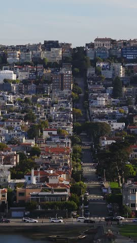 Aerial view looking up a steep urban street lined with townhouses and apartment buildings across the hilly Marina District and Pacific Heights in San Francisco.