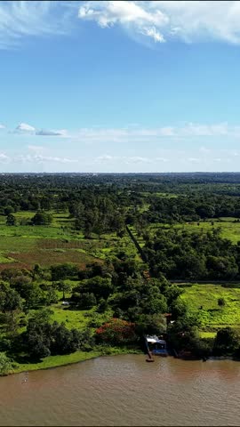 Vertical 9:16 aerial drone view over a wide lake and lush rural landscape with green fields, farmland, scattered properties and boats navigating near the shoreline under a bright blue sky.
