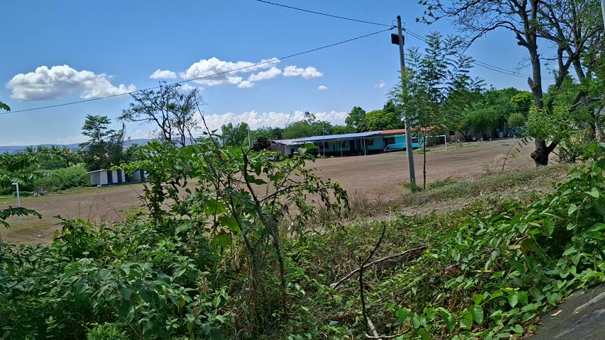 Rural dirt soccer field with small rustic adobe house and metal roof under blue sky