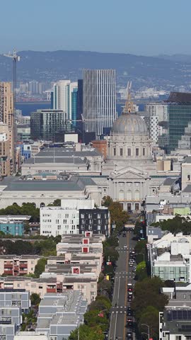 Aerial view reveals San Francisco City Hall along Fulton Street, surrounded by civic center architecture, vehicular traffic, and downtown buildings stretching toward the distant bay.