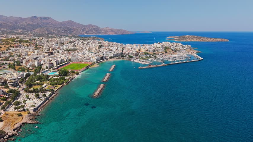 Aerial view of coastal town Agios Nikolaos in Crete, Greece, showing marina filled with boats and turquoise bay water along shoreline
