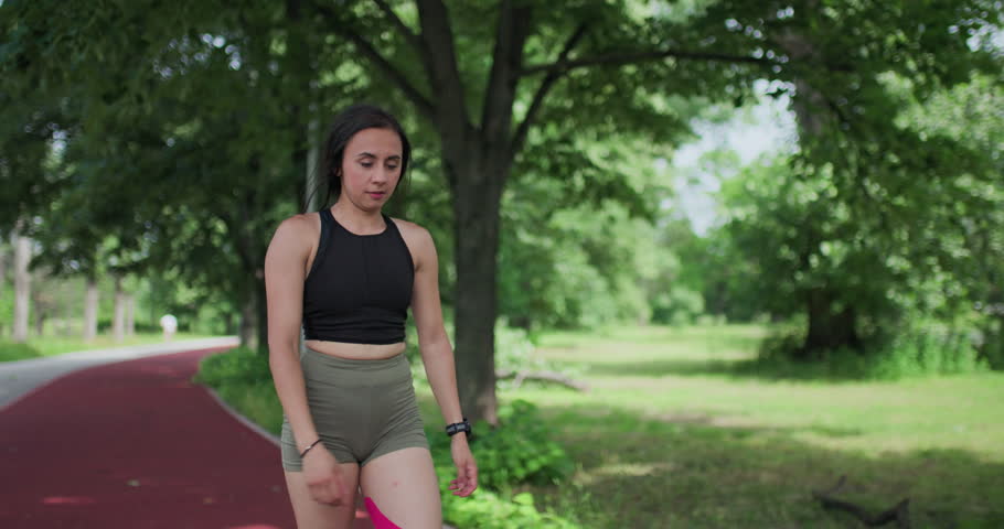 Athlete pauses on a running track, bending over with knee pain, showing kinesiology tape for injury support and recovery during outdoor exercise.