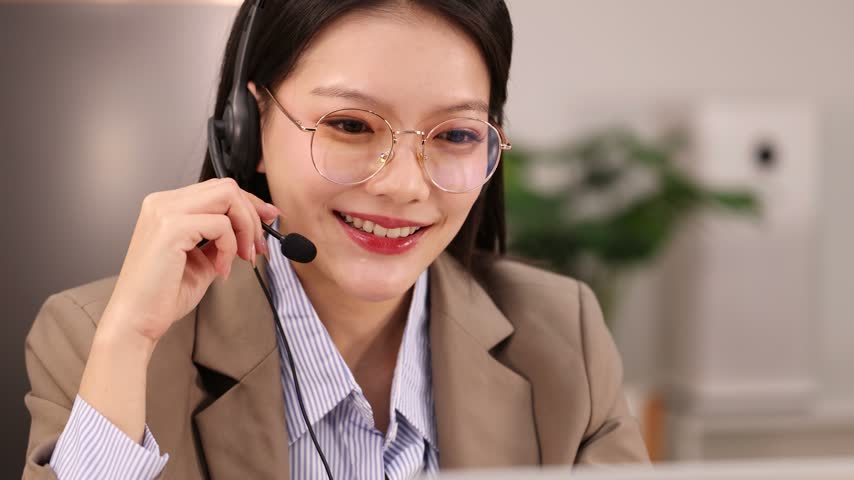 An Asian female customer service agent wearing a headset talks during an online meeting.
