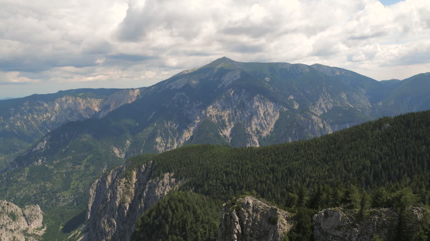 Clouds drift over peaks while light shifts across the rocky landscape and trees.