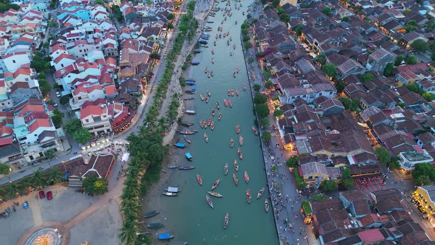 Soft twilight glow illuminates the historic riverside architecture as small wooden boats glide through the tranquil waters of Hoi An in Vietnam