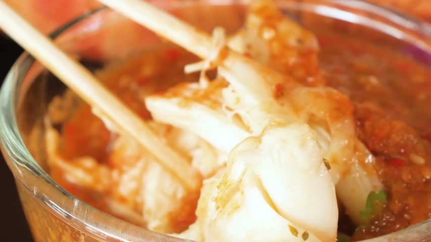 A detailed macro shot captures succulent, tender chunks of fresh white lobster meat being lifted with wooden chopsticks and coated in a vibrant, thick red chili sauce.
