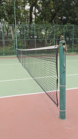 a green tennis court, featuring a wire metal basket filled with piles of yellow tennis balls in the lower right foreground.