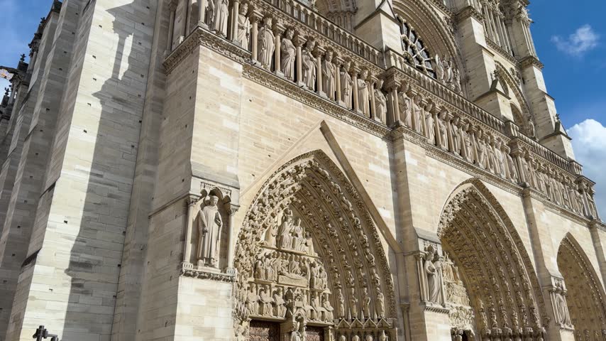 Low-angle upward shot of historic Notre Dame Cathedral beneath blue sky in Paris.