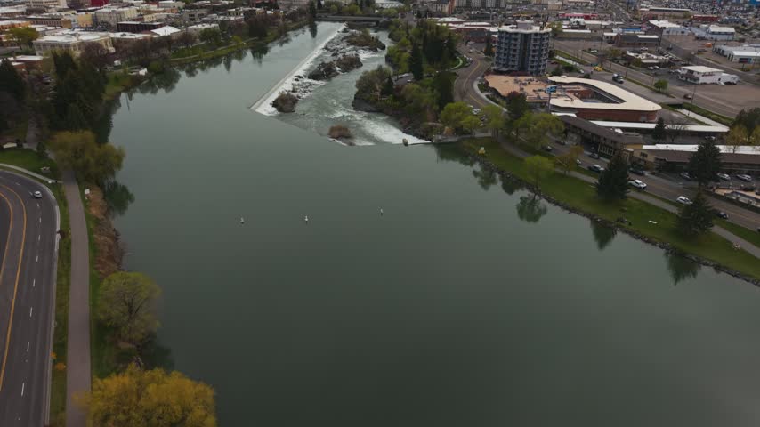 Aerial descent from a wide view of downtown Idaho Falls buildings along the Snake River down to the falls and weir on a spring day, Idaho, USA